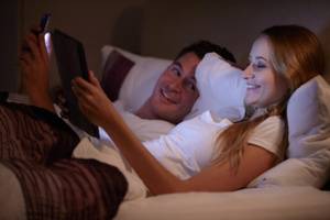 Couple Lying In Bed Using Digital Tablet And Mobile Phone